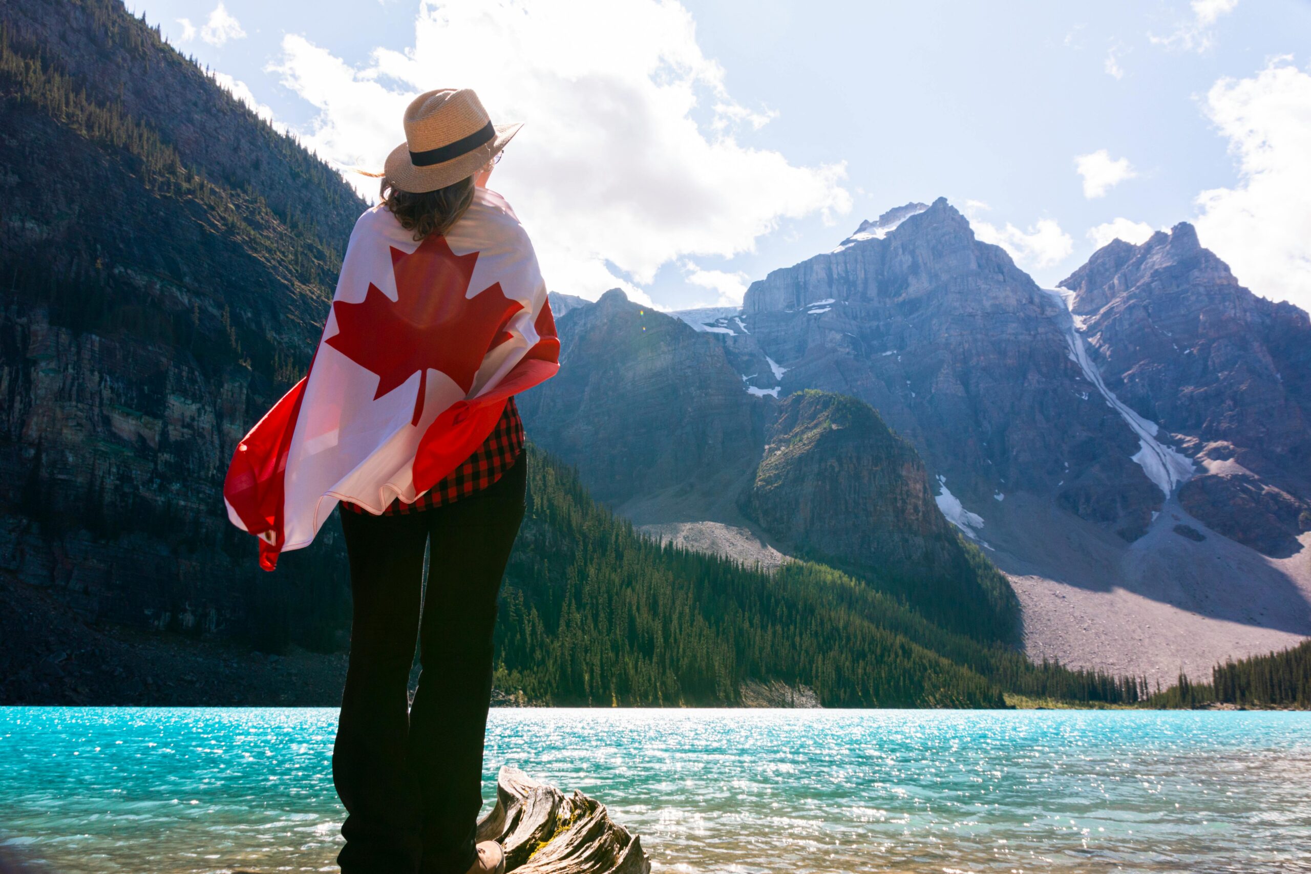 A woman stands wrapped in a Canadian flag, admiring the scenic Moraine Lake and mountains.
