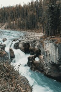 Captivating waterfall flowing through rugged rocks and lush forest in Jasper National Park, Canada.